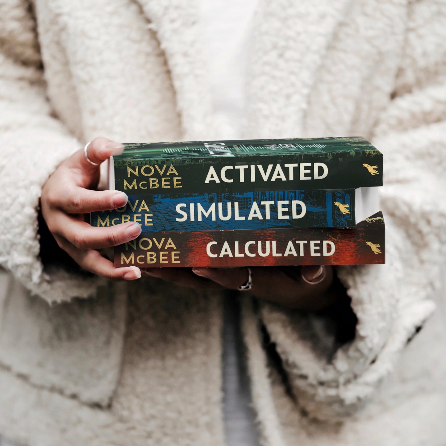 Person holding books titled 'Activated', 'Simulated', and 'Calculated' by Nova McBee.